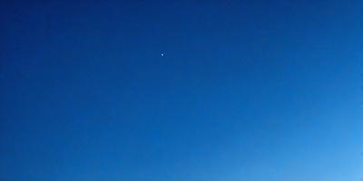 The primary subject of the image is a bright star in the night sky. The setting is a clear blue sky, with no clouds or other obstructions visible. The visual style is a photo, capturing the star and its surroundings in a natural and unaltered manner. The colors and mood of the image are predominantly blue, creating a serene and peaceful atmosphere.