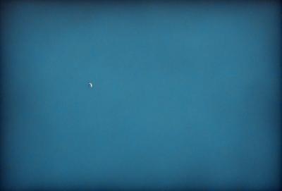The primary subject of the image is the moon, which is visible in the sky. The setting is a clear blue sky, and the visual style is a photo. The colors and mood of the image are predominantly blue, creating a calm and serene atmosphere.
