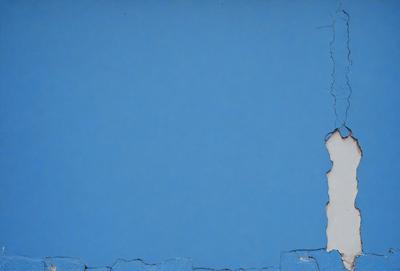 The primary subject of the image is a blue wall with a crack in it. The setting is an indoor environment, possibly a room or a building. The visual style is a photo, capturing the crack in the blue wall. The dominant colors are blue and white, creating a calm and serene atmosphere.
