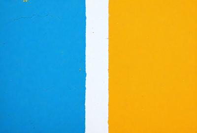 The primary subject of the image is a blue and yellow wall. The setting is a room with a blue wall and a yellow wall, creating a contrast between the two colors. The visual style is a close-up of the wall, showcasing the vibrant colors. The dominant colors are blue and yellow, creating a lively and energetic atmosphere.