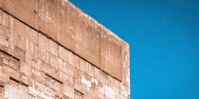 The primary subject of the image is a large, old, and worn-out brick wall. The setting is a blue sky, which serves as the backdrop for the wall. The visual style of the image is a photo, capturing the brick wall and the sky in a realistic manner. The colors in the image are predominantly blue, with the sky being the main color, and the brick wall being a mix of brown and white. The overall atmosphere of the image is calm and serene, with the brick wall standing tall against