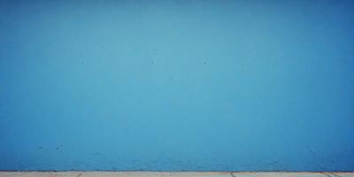 The primary subject of the image is a blue wall with a few white spots on it. The setting is an outdoor environment, possibly a beach or a poolside. The visual style is a photo, capturing the blue wall and its unique texture. The colors and mood of the image are predominantly blue, creating a calm and serene atmosphere.