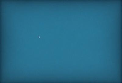 The primary subject of the image is a small planet or moon, which is located in the middle of the scene. The setting is a vast, dark blue sky, which serves as the backdrop for the planet. The visual style of the image is a photo, capturing the beauty of the celestial object against the expansive sky. The colors and mood of the image are predominantly dark and moody, with the blue sky providing a sense of depth and vastness.