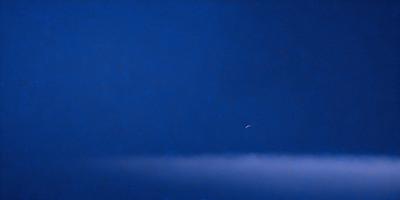 The primary subject of the image is a moon, which is seen in the sky. The setting is a dark blue sky, and the visual style appears to be a photo. The colors and mood of the image are predominantly dark and moody, with the moon being the main focal point.