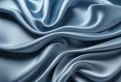 The primary subject of the image is a close-up of a blue fabric, possibly silk, with a flowing and swirling pattern. The setting is a blue background, which complements the blue fabric. The visual style is a close-up of the fabric, showcasing its texture and pattern. The colors and mood of the image are predominantly blue, creating a calm and serene atmosphere.