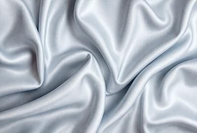 The primary subject of the image is a close-up of a piece of fabric, possibly a silk sheet or a piece of clothing. The setting is a white background, which highlights the fabric's texture and color. The visual style appears to be a photo, as it captures the details of the fabric. The colors and mood of the image are predominantly white, giving it a clean and elegant appearance.