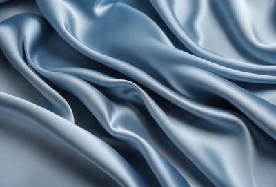 The primary subject of the image is a blue fabric, which appears to be a piece of silk. The setting is a close-up view of the fabric, showcasing its texture and details. The visual style is a realistic representation of the fabric, capturing its natural appearance. The colors and mood of the image are predominantly blue, creating a calm and serene atmosphere.