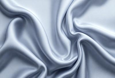 The primary subject of the image is a close-up of a piece of fabric, likely silk, with a blue hue. The setting is a white background, which provides a clean and minimalist appearance. The visual style is a close-up, focusing on the intricate details of the fabric. The colors and mood of the image are predominantly blue, creating a calm and serene atmosphere.