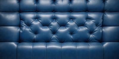 The primary subject of the image is a blue couch with a leather-like texture. The setting is a room with a blue wall, and the visual style is a close-up of the couch. The colors and mood of the image are predominantly blue, creating a calm and relaxing atmosphere.