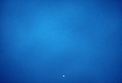 The primary subject of the image is a blue sky with a single white dot in the middle of it. The sky appears to be cloudless, and the white dot is the only visible object in the scene. The visual style of the image is a photo, and the colors and mood are predominantly blue and calm.