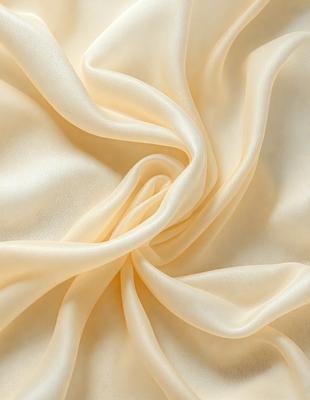 The primary subject of the image is a piece of fabric, possibly a silk or satin material, with a yellowish hue. The fabric is draped over a surface, creating a flowing and elegant appearance. The setting appears to be a room with a white background, which contrasts with the yellow fabric. The visual style of the image is a close-up of the fabric, showcasing its texture and color. The overall atmosphere of the image is elegant and sophisticated, with the yellow fabric adding a touch
