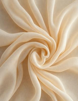 The primary subject of the image is a large piece of fabric, possibly a sheet or a curtain, with a swirling pattern. The fabric is cream-colored and appears to be made of silk. The setting is a white background, which provides a clean and minimalist look to the image. The visual style is a close-up of the fabric, showcasing its texture and pattern. The colors and mood of the image are warm and elegant, with the cream-colored fabric creating a sense of lux