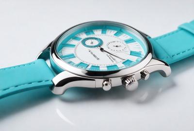 The primary subject of the image is a blue watch with a white face. The watch is placed on a white surface, which creates a clean and minimalist appearance. The visual style of the image is a close-up of the watch, highlighting its details and design. The colors and mood of the image are predominantly blue and white, giving it a calm and sophisticated feel.