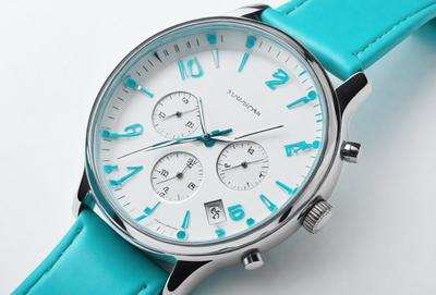 The primary subject of the image is a watch with a blue band. The watch is placed on a white surface, which serves as the background. The visual style of the image is a photo, capturing the details of the watch and its band. The colors and mood of the image are predominantly blue, giving it a calm and soothing atmosphere.
