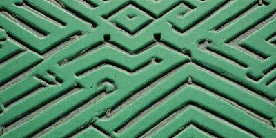 The primary subject of the image is a green, patterned floor with a maze-like design. The setting is indoors, possibly in a room with a green carpet. The visual style is a close-up of the floor, showcasing the intricate pattern. The colors and mood of the image are predominantly green, creating a calm and serene atmosphere.