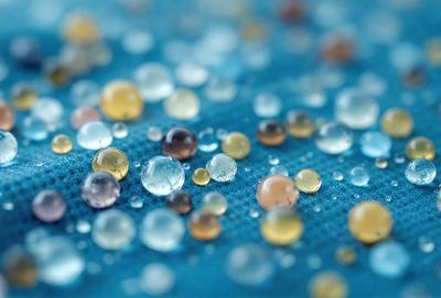 The primary subject of the image is a close-up of a blue surface with a variety of small, colorful beads or droplets scattered across it. The setting appears to be a blue cloth or a similar material. The visual style of the image is a close-up, which emphasizes the details of the beads and their arrangement on the surface. The colors and mood of the image are vibrant and lively, with the blue cloth providing a contrasting background for the colorful beads.