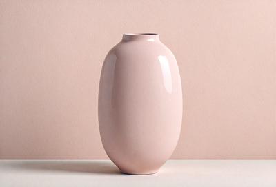 The primary subject of the image is a pink vase, which is the main object, scene, or focus of the image. The vase is placed on a table, which serves as the setting or background. The visual style of the image is a photo, capturing the vase in its natural environment. The colors and mood of the image are predominantly pink, creating a warm and inviting atmosphere.