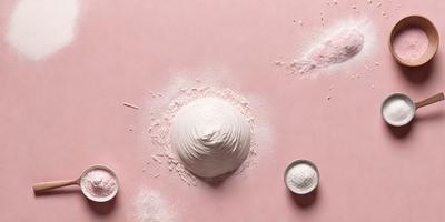 The primary subject of the image is a large, white, fluffy ball of dough, which is placed on a pink surface. The dough appears to be a mixture of flour and water, and it is being prepared for baking. The setting is a kitchen, with a bowl visible in the background. The visual style is a close-up of the dough, showcasing its texture and appearance. The colors and mood of the image are predominantly pink, which gives the scene a warm and