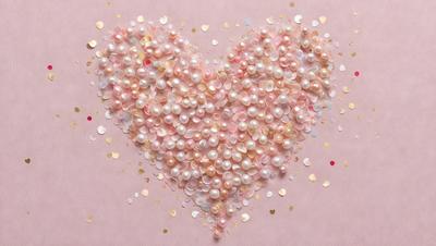 The primary subject of the image is a heart-shaped arrangement of pearls. The heart is made up of various pearls of different sizes, creating a visually appealing and elegant display. The setting is a pink background, which adds a touch of warmth and softness to the scene. The visual style of the image is a close-up of the heart, emphasizing the details of the pearls and their arrangement. The colors and mood of the image are predominantly pink, which is associated