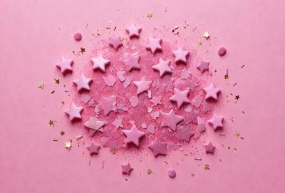 The primary subject of the image is a pink background with a sprinkling of pink stars. The setting is a pink table, and the visual style is a combination of photo and digital art. The dominant colors are pink and gold, creating a warm and inviting atmosphere.