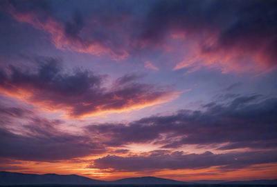 The primary subject of the image is a beautiful sunset, with the sun setting behind a cloudy sky. The setting is a mountainous landscape, with mountains visible in the distance. The visual style of the image is a photo, capturing the stunning colors and atmosphere of the sunset. The dominant colors are orange, red, and yellow, creating a warm and serene mood.