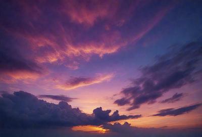 The primary subject of the image is a beautiful sunset, with the sun setting behind a cloudy sky. The setting is a cloudy sky, and the visual style is a photo. The colors and mood of the image are dominated by warm hues, creating a serene and peaceful atmosphere.