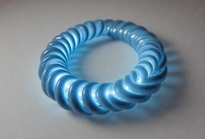 The primary subject of the image is a blue spiral ring. The setting is a white surface, and the visual style appears to be a photo. The dominant colors are blue and white, creating a calm and serene atmosphere.