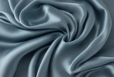 The primary subject of the image is a close-up of a blue fabric, possibly a piece of silk. The setting is a dark background, which emphasizes the fabric's texture and color. The visual style appears to be a close-up photo of the fabric. The colors and mood of the image are predominantly blue, creating a calm and serene atmosphere.