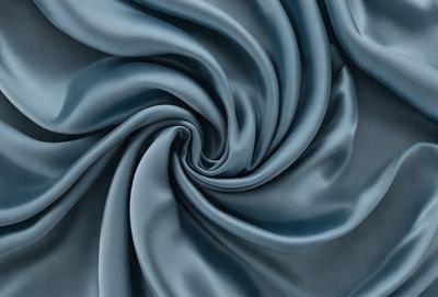 The primary subject of the image is a blue fabric, which appears to be a piece of silk. The setting is a dark background, which contrasts with the blue fabric. The visual style is a close-up of the fabric, showcasing its texture and pattern. The colors and mood of the image are predominantly blue, creating a calm and serene atmosphere.