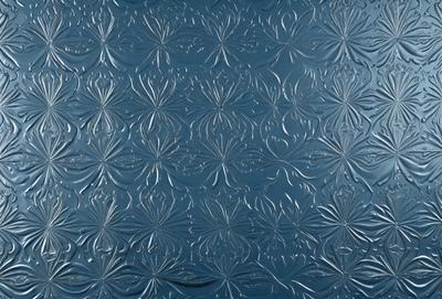 The primary subject of the image is a blue glass tile with a pattern of flower designs. The setting is a wall, and the visual style is a combination of photo and digital art. The dominant colors are blue and silver, creating a calm and soothing atmosphere.