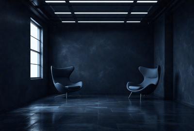 The primary subject of the image is a room with two chairs, one on the left side and the other on the right side. The setting is a dark room with a blue wall, which creates a moody atmosphere. The visual style is a black and white photo, giving the image a classic and timeless appearance. The colors and mood of the image are predominantly dark and dramatic, with the blue wall adding a touch of contrast to the overall scene.