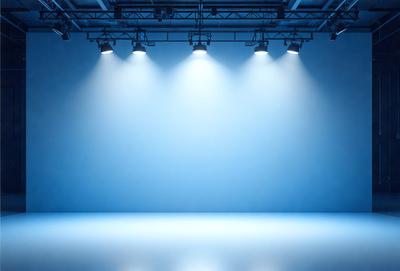 The primary subject of the image is a blue background with a row of lights shining on it. The setting is a stage or a theater, with the lights creating a dramatic atmosphere. The visual style is a combination of digital art and photography, as the lights are captured in a way that highlights their brightness and creates a striking contrast against the blue background. The colors and mood of the image are predominantly blue, with the lights adding a touch of warmth and energy to the scene.