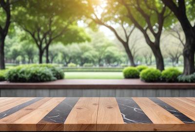 The primary subject of the image is a wooden table with a black and white checkered pattern. The table is placed in a park setting, surrounded by trees and grass. The visual style of the image is a photo, capturing the natural environment and the table's design. The colors and mood of the image are predominantly green and serene, with the wooden table and the natural surroundings creating a peaceful and inviting atmosphere.