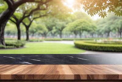 The primary subject of the image is a wooden countertop with a marble top. The setting is a park with trees and grass in the background. The visual style is a photo, and the colors and mood are natural and serene.