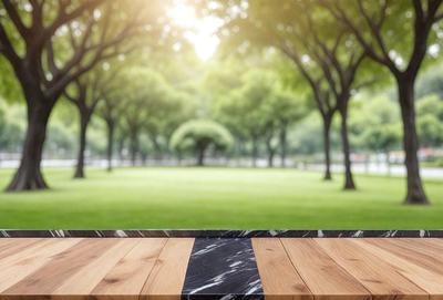 The primary subject of the image is a wooden table with a black and white marble top. The table is placed in a grassy area surrounded by trees, creating a serene and natural setting. The visual style of the image is a photo, capturing the beauty of the outdoor environment and the wooden table. The colors and mood of the image are predominantly green and calm, reflecting the peaceful atmosphere of the scene.
