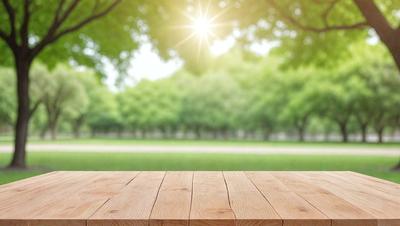 The primary subject of the image is a wooden table, which is the main object in the scene. The table is placed in a grassy field, surrounded by trees. The visual style of the image is a photo, capturing the natural environment and the wooden table. The colors and mood of the image are predominantly green, with the grassy field and trees creating a serene and peaceful atmosphere.