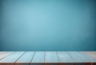 The primary subject of the image is a wooden table with a blue surface. The table is placed against a blue wall, creating a visually appealing contrast. The setting appears to be a room with a clean and organized appearance. The visual style of the image is a photo, capturing the details of the wooden table and the blue wall. The colors and mood of the image are predominantly blue, giving it a calm and serene atmosphere.