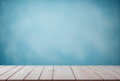 The primary subject of the image is a wooden table with a blue background. The table is positioned in front of a blue wall, creating a visually appealing contrast. The visual style of the image is a photo, capturing the wooden table and the blue wall in a realistic manner. The colors and mood of the image are predominantly blue, giving it a calm and serene atmosphere.