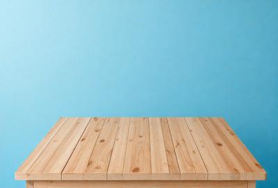 The primary subject of the image is a wooden table. The table is placed against a blue wall, creating a contrasting backdrop. The visual style of the image is a photo, showcasing the wooden table and its surroundings. The colors and mood of the image are predominantly blue, giving it a calm and serene atmosphere.