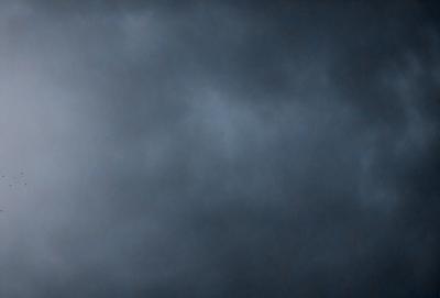 The primary subject of the image is a cloudy sky. The setting is a dark, cloudy day with a gloomy atmosphere. The visual style is a photo, capturing the natural beauty of the cloudy sky. The colors and mood are predominantly dark and moody, with the clouds casting a shadow over the landscape.
