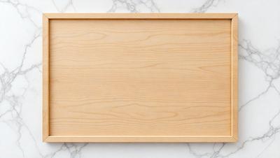 The primary subject of the image is a wooden tray or board. The setting is a marble countertop, which serves as the background. The visual style is a photo, capturing the wooden tray in its natural environment. The colors and mood of the image are predominantly neutral, with the wooden tray being the main focus.