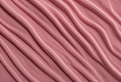 The primary subject of the image is a close-up of a pink fabric with a wavy pattern. The setting is a pink background, which adds to the overall visual style. The image is a photo, showcasing the fabric's texture and pattern. The dominant colors are pink and red, creating a warm and inviting atmosphere.