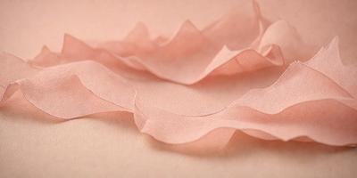 The primary subject of the image is a pink piece of fabric, which is the main focus of the scene. The setting is a pink background, which complements the pink fabric. The visual style of the image is a close-up of the pink fabric, showcasing its texture and details. The colors and mood of the image are predominantly pink, creating a warm and inviting atmosphere.