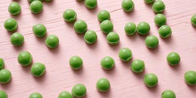 The primary subject of the image is a close-up of green peas, which are the main objects in the scene. The setting is a pink surface, which serves as the background. The visual style of the image is a close-up of the peas, showcasing their texture and details. The colors in the image are predominantly green, which gives the image a fresh and natural atmosphere.
