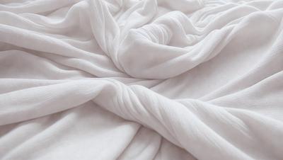 The primary subject of the image is a white sheet or blanket, which is the main object, scene, or focus of the image. The setting or background is a bed, and the visual style is a photo. The colors and mood of the image are predominantly white, giving it a clean and serene atmosphere.