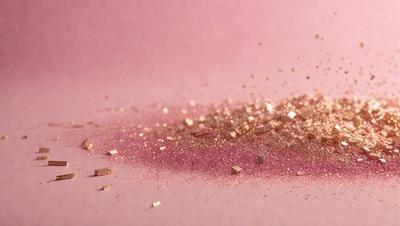 The primary subject of the image is a pink surface with gold glitter sprinkled on it. The setting appears to be a table or a similar surface. The visual style of the image is a close-up of the glitter on the pink surface, which gives it a textured and shiny appearance. The colors and mood of the image are predominantly pink and gold, creating a warm and inviting atmosphere.