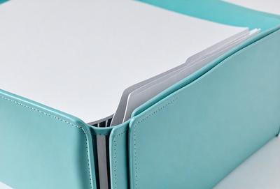 The primary subject of the image is a blue book with a white interior. The book is open and appears to be a notebook. The setting is a white surface, which provides a clean and minimalist background for the book. The visual style is a photo, capturing the details of the book and its interior. The colors and mood of the image are predominantly blue and white, creating a calm and organized atmosphere.