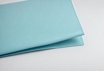 The primary subject of the image is a blue leather wallet. The wallet is placed on a white surface, which serves as the background. The visual style of the image is a photo, capturing the details of the wallet. The dominant colors in the image are blue and white, creating a calm and soothing atmosphere.