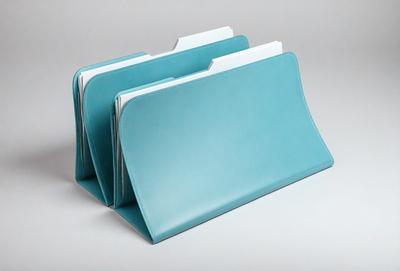 The primary subject of the image is a stack of three blue folders. The folders are placed on a white surface, which serves as the setting and background of the image. The visual style of the image is a photo, capturing the details of the folders and the white surface. The colors and mood of the image are predominantly blue, giving it a calm and organized appearance.