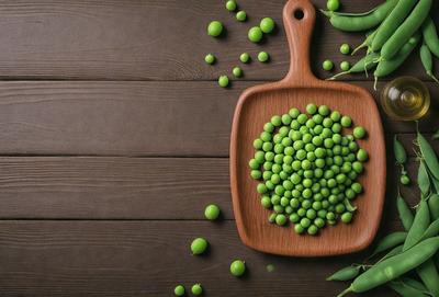 The primary subject of the image is a wooden serving tray filled with green peas. The tray is placed on a wooden table, which serves as the setting and background of the scene. The visual style of the image is a photo, capturing the natural colors and textures of the peas and the wooden serving tray. The colors and mood of the image are predominantly green, reflecting the freshness and naturalness of the peas.